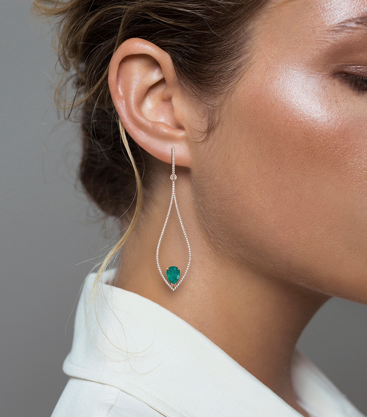 Woman wearing the Oliver Heemeyer 18k rose gold chandelier earrings, adorned with numerous diamonds and refined with two drop shaped Colombian emeralds.